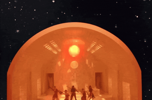 a group of people are dancing in a room with a large orange object in the background