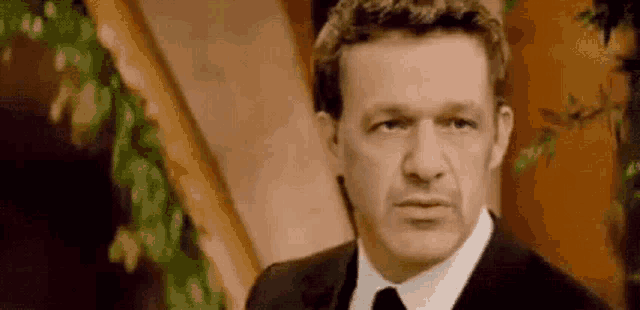 a man in a suit and tie is making a funny face and looking at the camera .