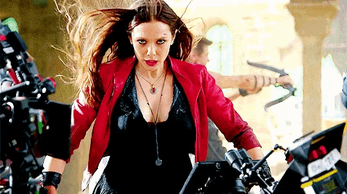 a woman in a red jacket and black top is standing next to a camera