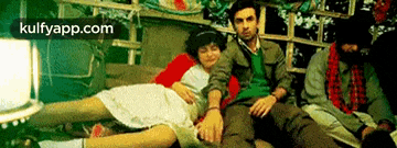 a group of people are sitting on a couch holding hands and a woman is laying on a man 's lap .