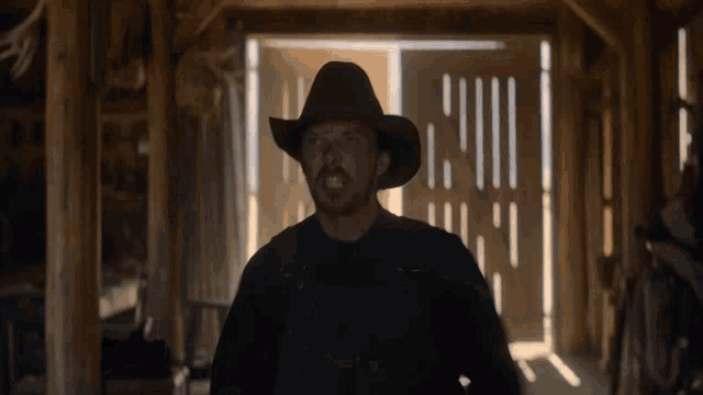 a man in a cowboy hat stands in front of a barn door