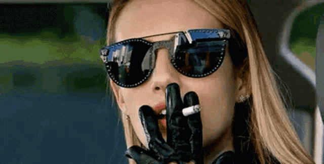 a woman wearing sunglasses is smoking a cigarette in a car .