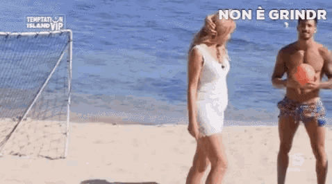 a woman in a white dress is standing next to a shirtless man on a beach holding a ball .