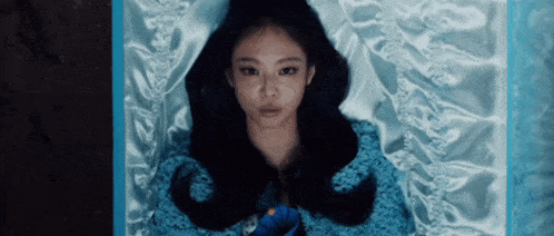 a woman is laying in a blue coffin holding a blue flower .