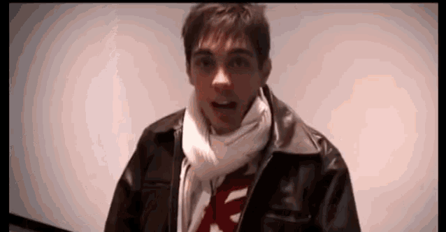 a man wearing a scarf and a leather jacket is looking at the camera