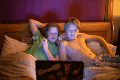 a boy and a girl are laying on a bed looking at a laptop screen that says gettyimages on it