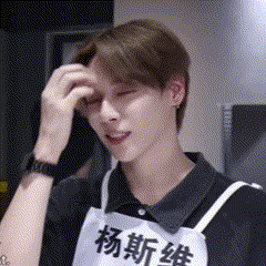 a man wearing a black shirt and an apron with chinese writing on it is scratching his head .