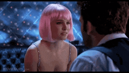 a man and a woman are looking at each other in a club . the woman has pink hair .