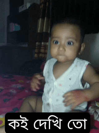 a baby in a white shirt is sitting on a bed next to a sign that says kae deshi ota