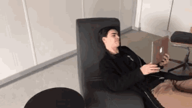 a man is laying in a chair with a laptop on his lap .