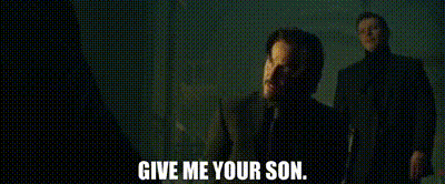 a man in a suit and tie is talking to another man in a dark room and says `` give me your son . ''