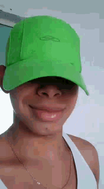 a man wearing a green hat is smiling and wearing a white tank top .