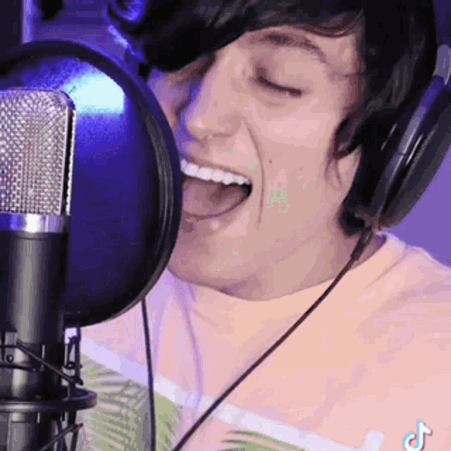 a man wearing headphones is singing into a microphone with his mouth open .