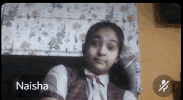 a girl named naisha is sitting in front of a floral wall