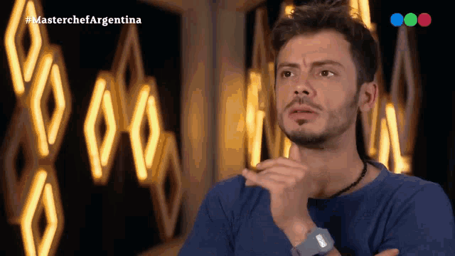 a man in a blue shirt is standing in front of a sign that says " masterchef argentina "
