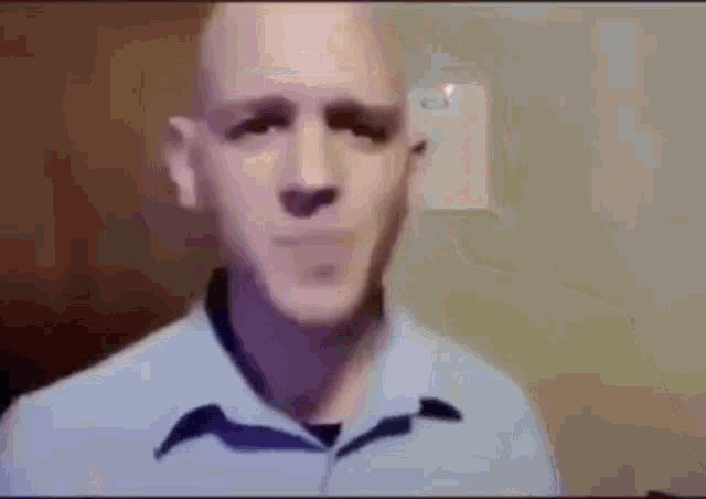 a bald man in a blue shirt is making a funny face while looking at the camera .