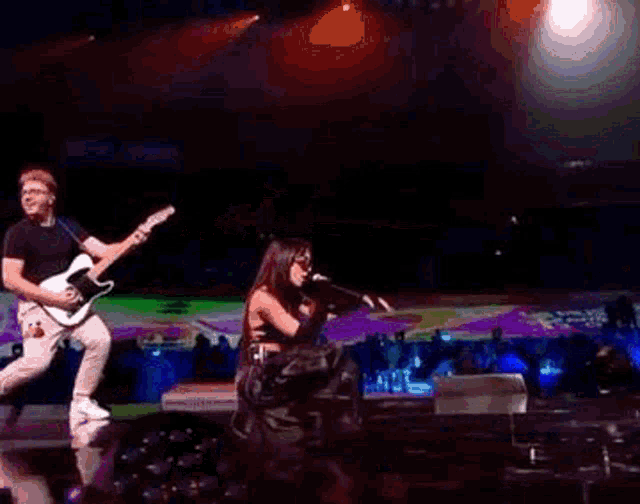 a man is playing a guitar while a woman sings into a microphone .