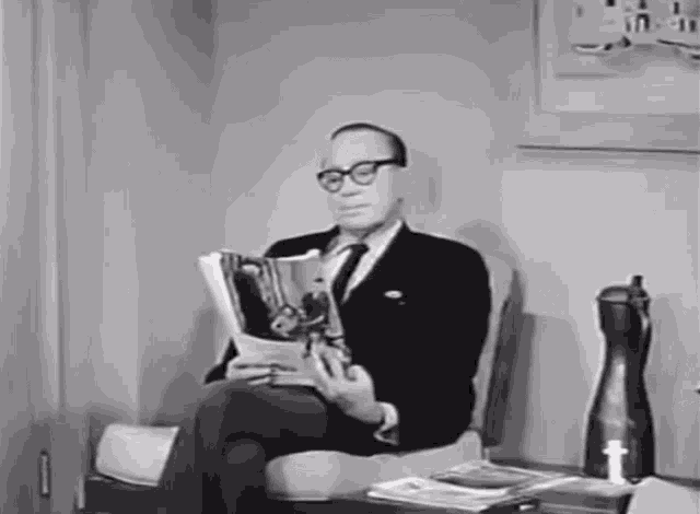 a man wearing glasses is reading a magazine
