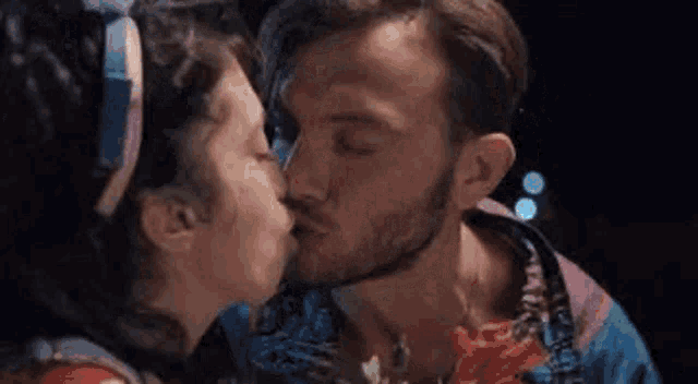a man and a woman are kissing in front of flowers .
