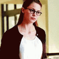 a woman wearing glasses and a white tank top is standing in a room .