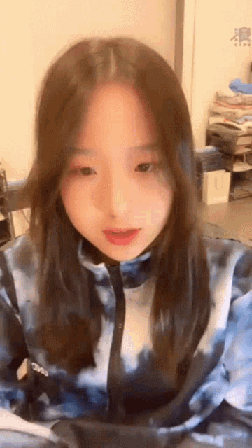 a girl with long hair is wearing a blue tie dye jacket and looking at the camera