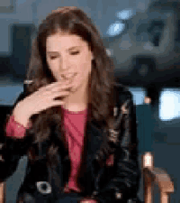 a woman is sitting in a chair with her hand on her face . she is wearing a leather jacket and a pink shirt .