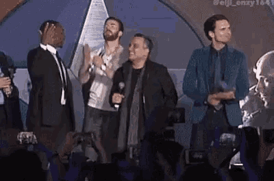 a group of men are standing on a stage in front of a microphone .