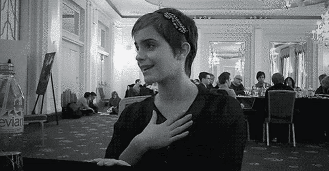 a black and white photo of a woman holding her hand to her chest in a room .