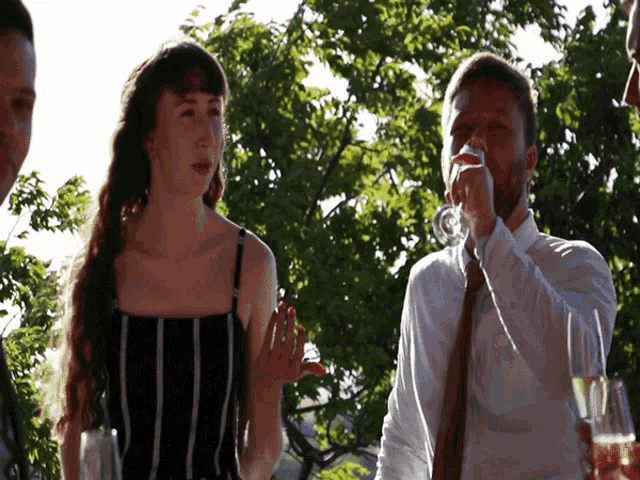 a man in a white shirt is drinking from a glass while standing next to a woman in a black and white striped dress