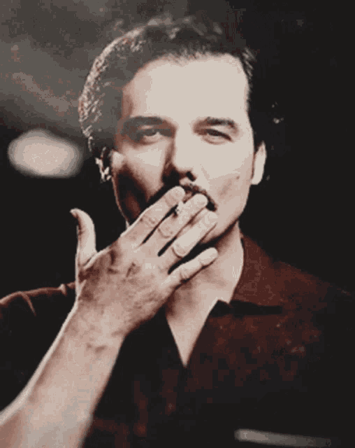 a man covering his mouth with his hand while smoking a cigar