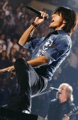 a man in a denim shirt is singing into a microphone on stage .