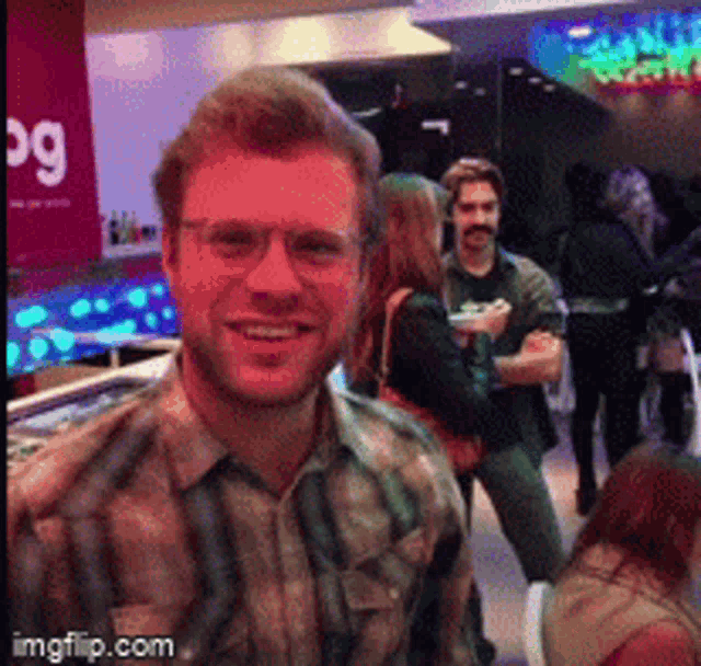 a man wearing glasses and a plaid shirt is smiling in front of a sign that says bg