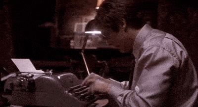a man is typing on a typewriter with a pen in his hand .