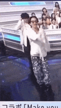 a man is dancing on a stage in front of a crowd with the words make you in the corner .