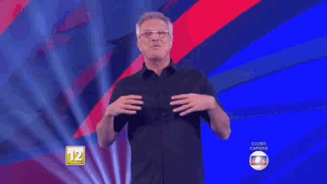 a man in a black shirt is standing in front of a blue and red background with the number 12 in the corner