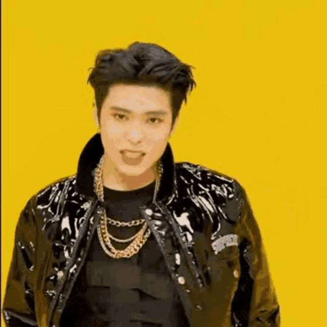 a man in a black jacket is standing in front of a yellow background and making a funny face .