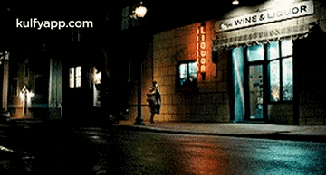 a woman walks down a street in front of a wine and liquor store