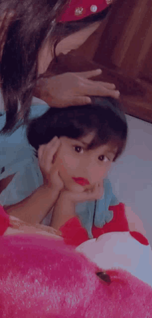 a woman petting a little girl 's head while she looks at the camera