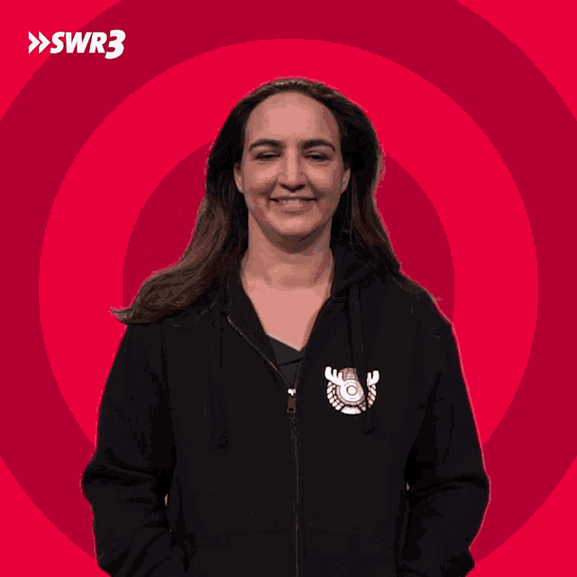 a woman wearing a black hoodie with a logo for swr3 waves her hand