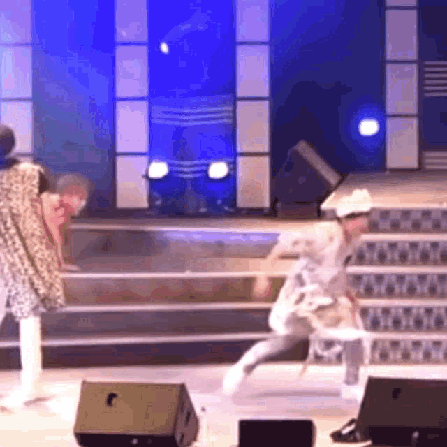 a group of people are dancing on a stage in front of a blue wall