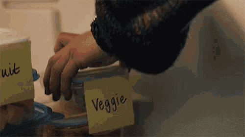 a person is putting a container of food in a refrigerator with a sticky note that says veggie .