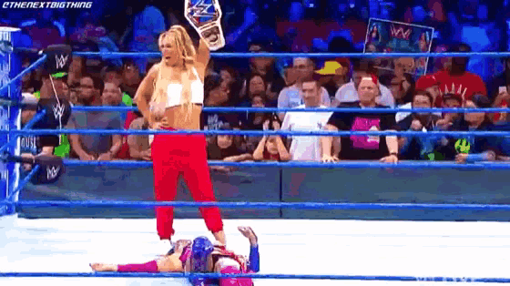 a woman is standing in a wrestling ring holding a championship while another woman is laying on the ground .