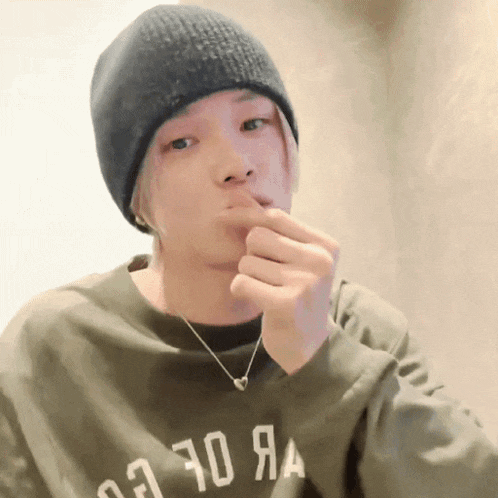a man wearing a beanie and a sweater with the number 70 on it holds his finger to his mouth