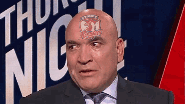 a man in a suit and tie with a sydney roosters logo on his head