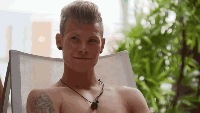 a shirtless man with a tattoo on his arm sits in a white chair
