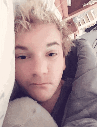 a young man with blonde hair is laying in a bed with his head on a pillow