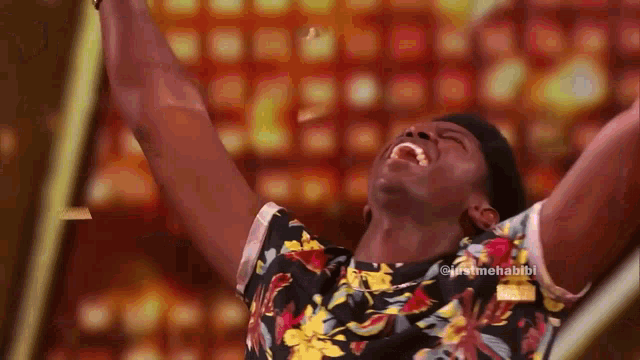 a man in a floral shirt is laughing with his arms up