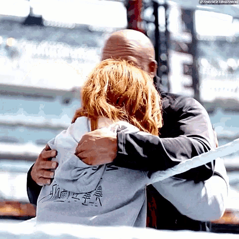 a man is hugging a woman who is wearing a grey sweatshirt with chinese writing on the back