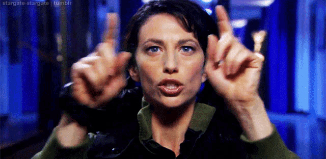 a woman in a green jacket is making a funny face with her hands in the air