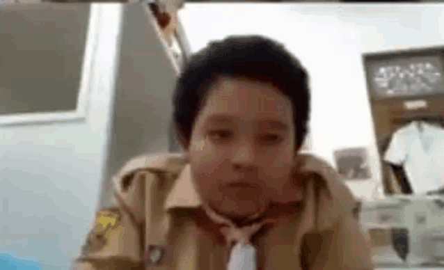 a young boy in a brown shirt and tie is sitting at a desk .